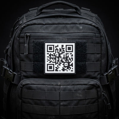 A black tactical backpack with a black-and-white QR code patch on the front, set against a dark background.